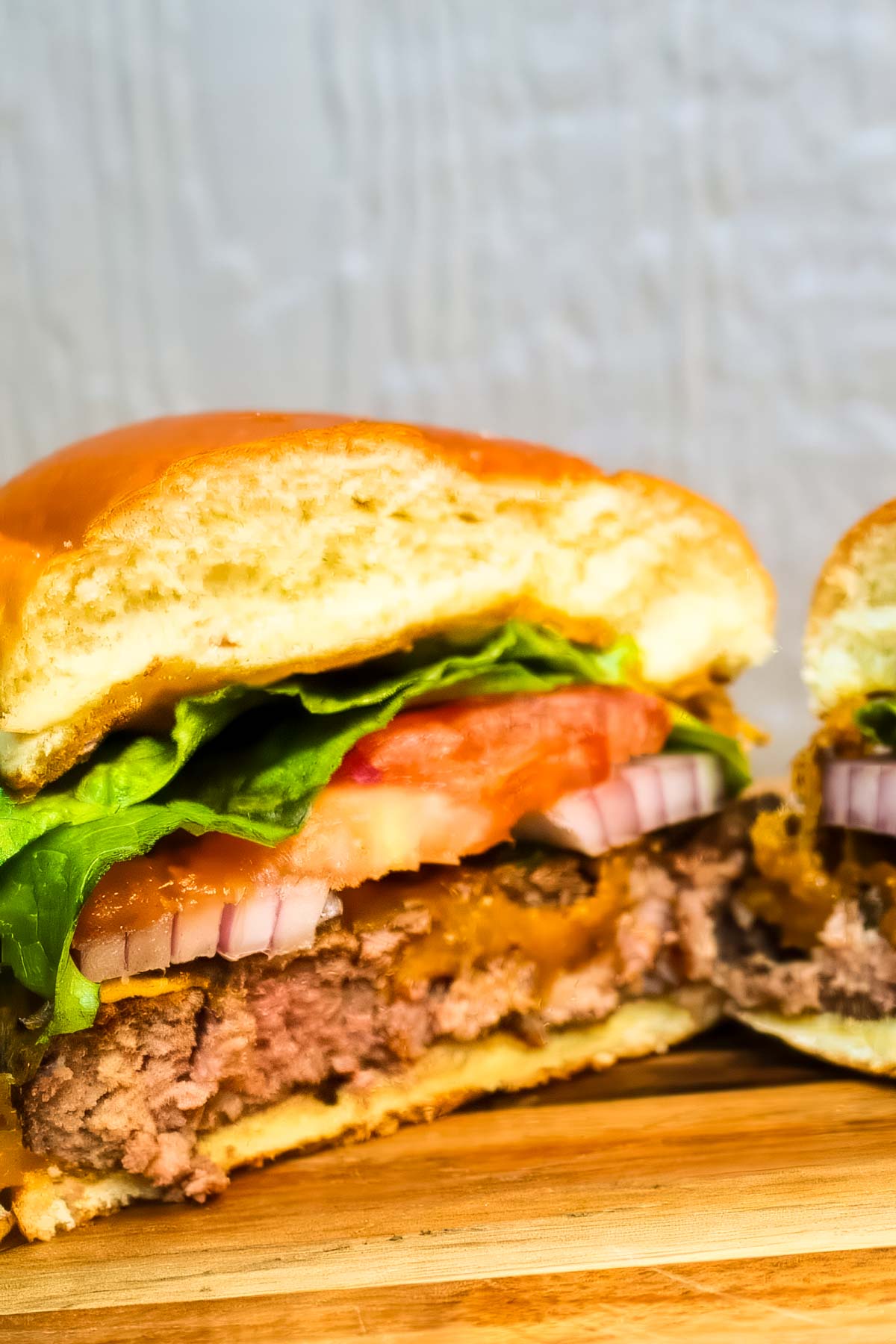Smoked Hamburgers a smoked hamburger that's been cut in half, showing the inside layers of bun, ground beef, red onion, tomato, and lettuce