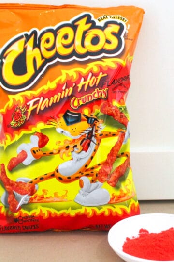 a bag of cheetos sitting upright next to a small white dish filled with a copycat version of flamin hot cheetos seasoning