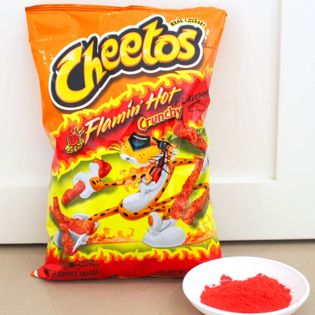 a bag of cheetos sitting upright next to a small white dish filled with a copycat version of flamin hot cheetos seasoning