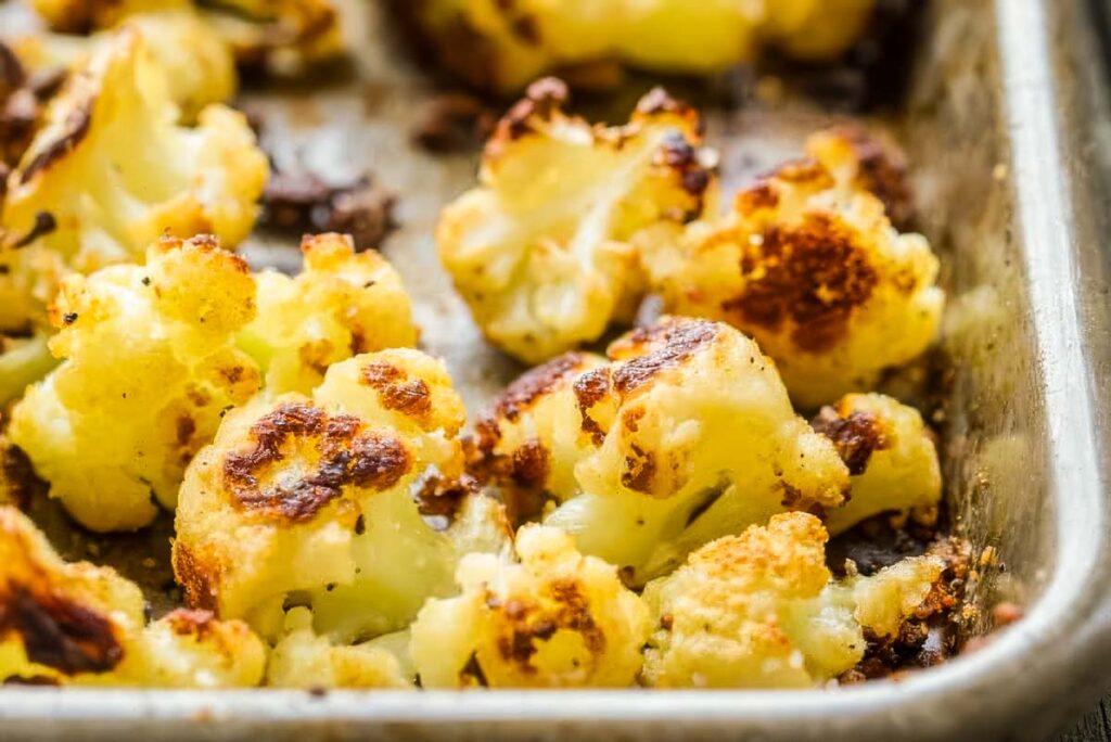Macro shot of roasted cauliflower with crispy, browned edges on a baking sheet.