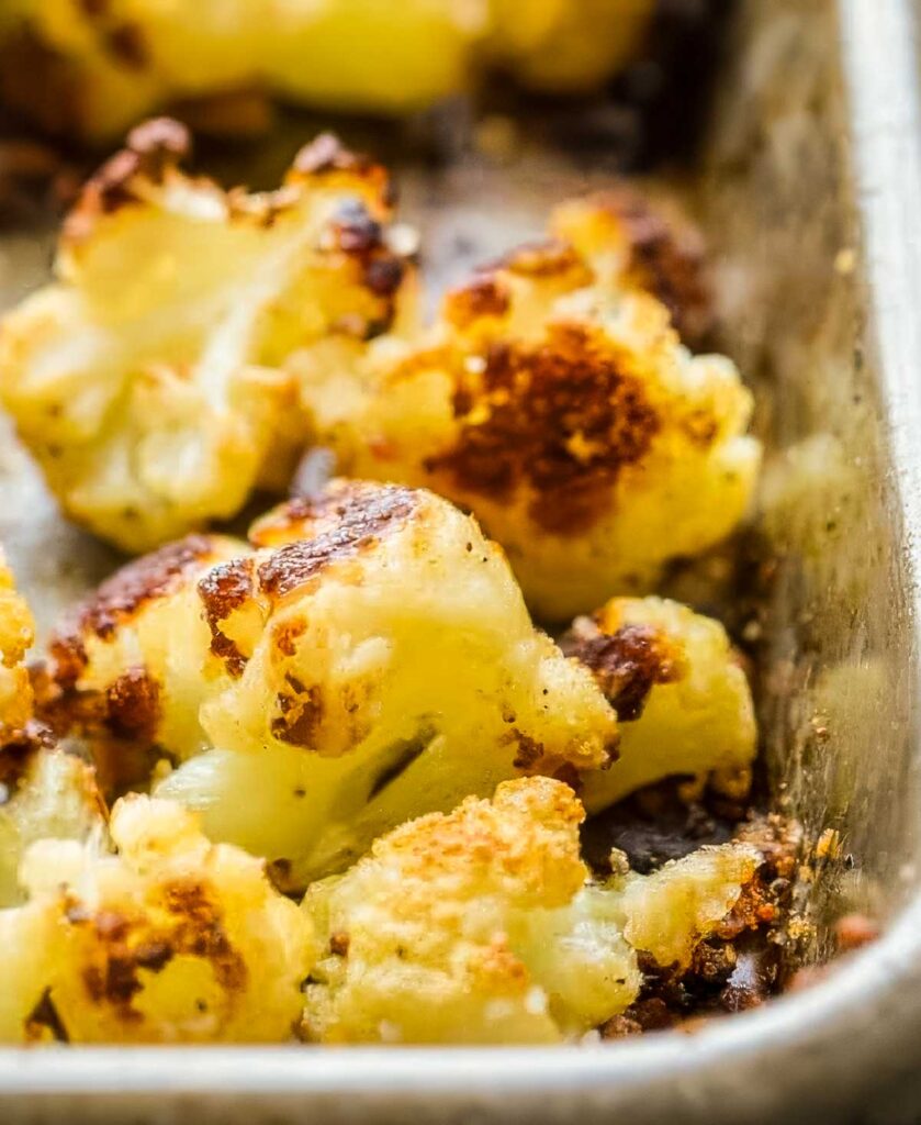 Close-up of golden, crispy roasted cauliflower nestled in the corner of a metal baking sheet.