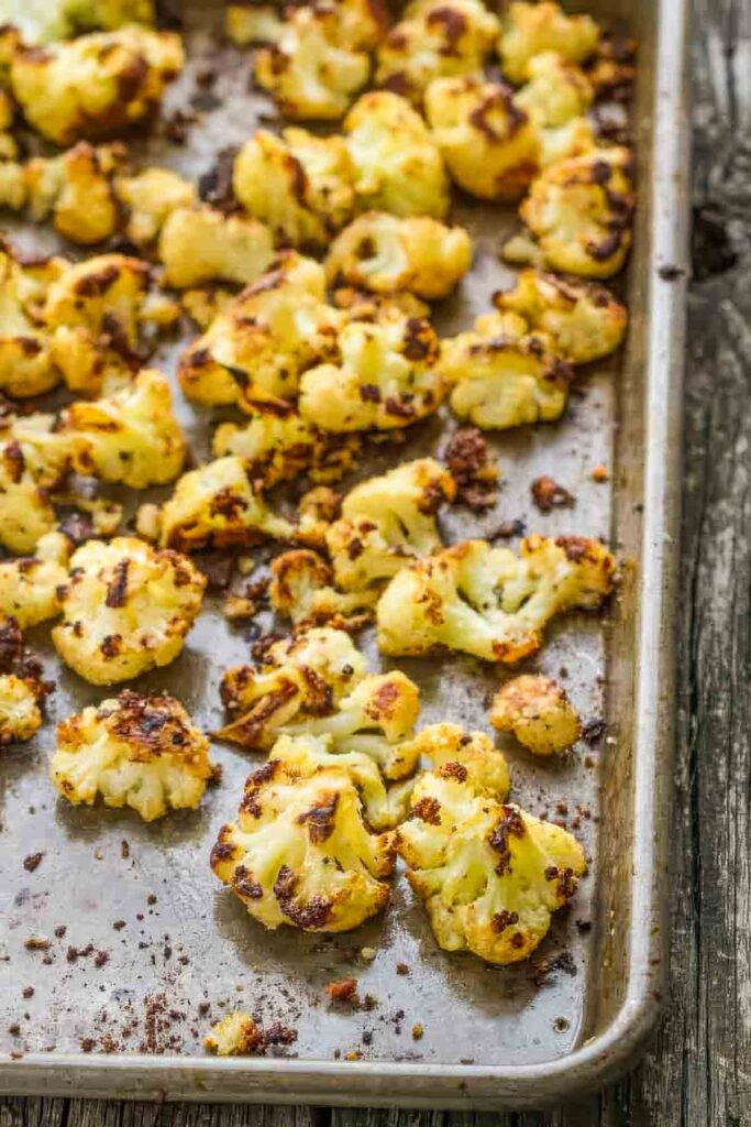 Baking sheet filled with parmesan roasted cauliflower florets with browned, crispy bits scattered throughout.