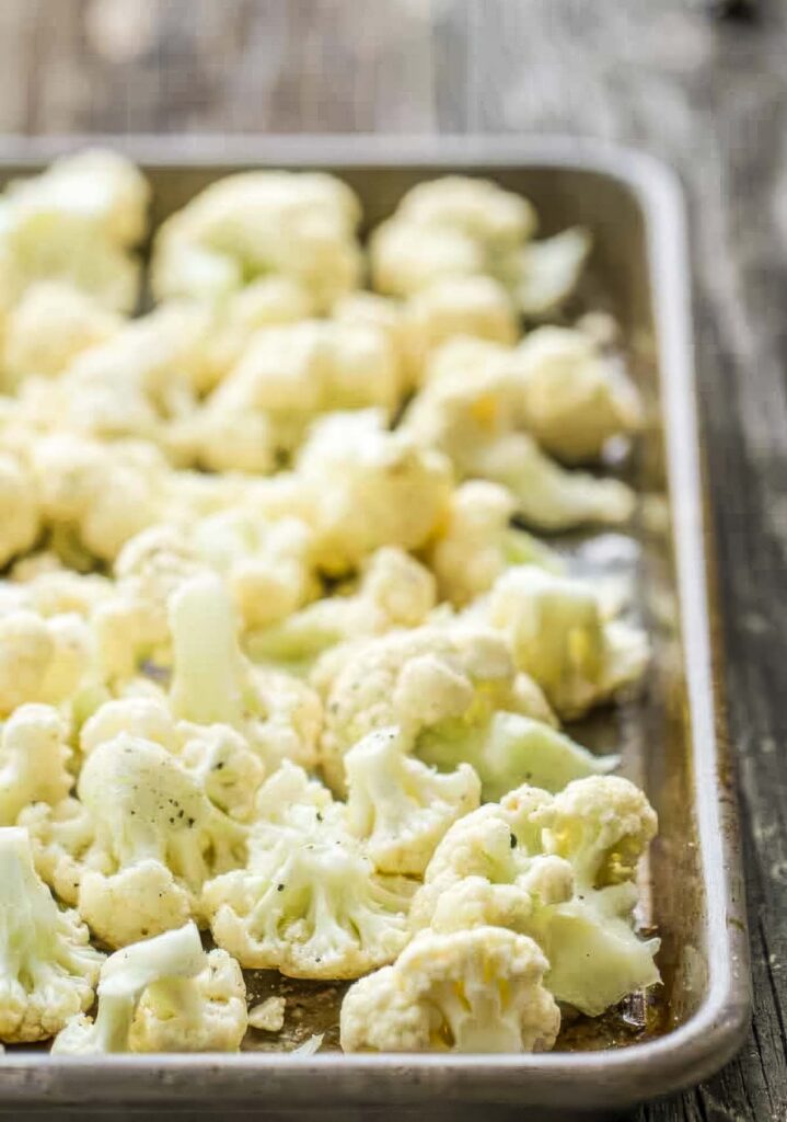 Raw cauliflower florets spread out on a sheet pan, lightly coated in olive oil and seasoning.