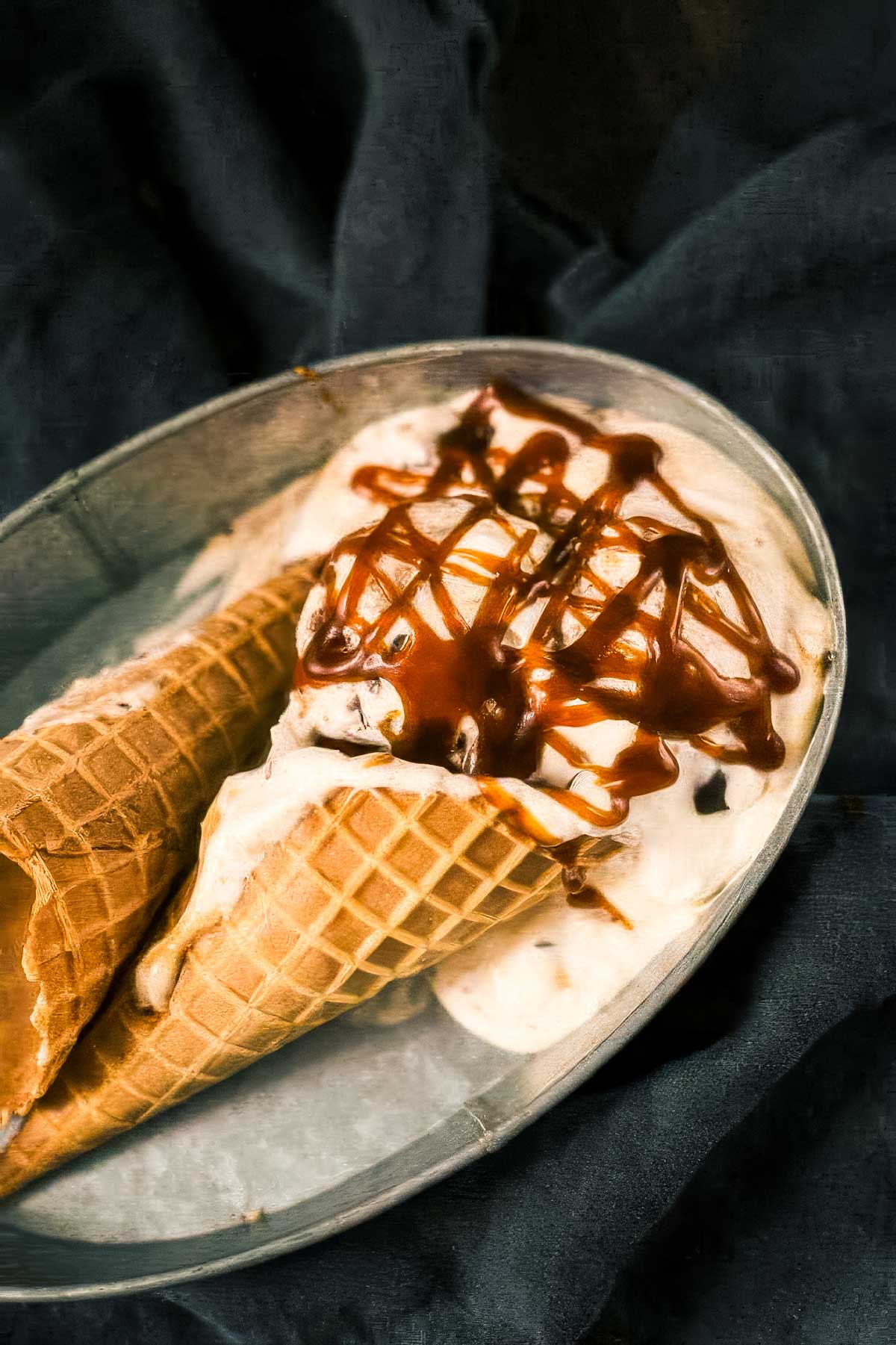 Chunky Monkey Ice Cream Recipe (No-Churn!) two ice cream cones from a chunky monkey ice cream recipe on their side in a vintage metal tin