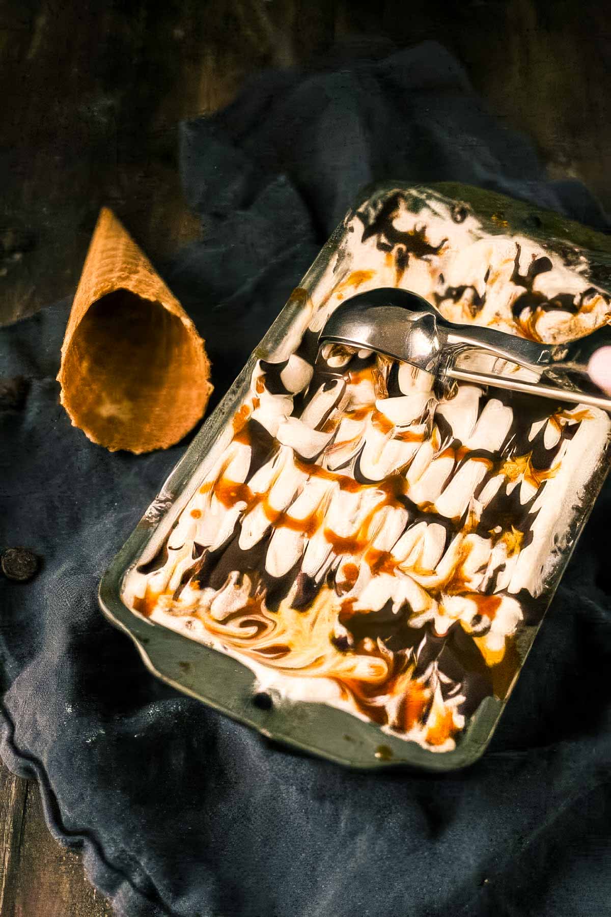 Chunky Monkey Ice Cream Recipe (No-Churn!) a metal loaf pan filled to the brim with chunky monkey ice cream, with an ice cream scoop sitting on the top and a waffle cone next to it