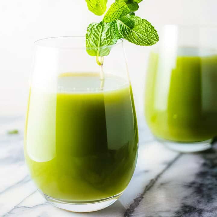 a glass of cucumber fruit juice with a sprig of fresh mint as garnish, with another glass of juice in the background