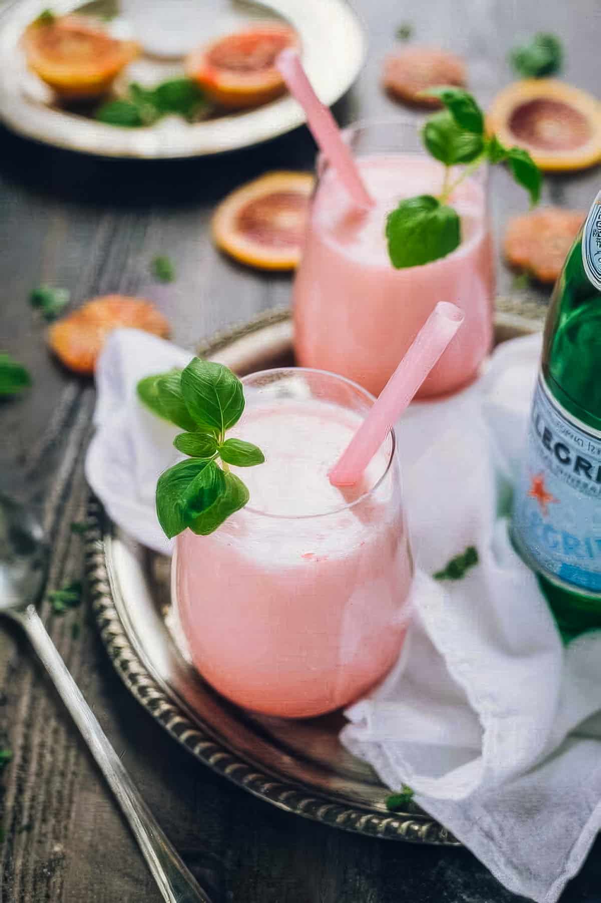 Italian Blood Orange Soda – Simple Party Drink Recipe two glasses of italian blood red soda garnished with fresh basil, on a tray next to a bottle of pellegrino and fresh blood orange slices
