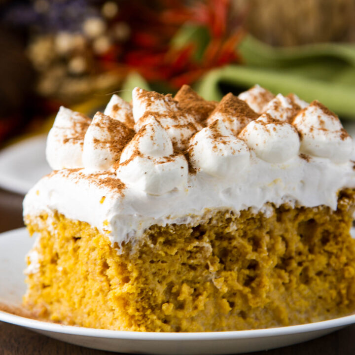 a slice of pumpkin tres leches cake on a small white plate on a wood table with fall decorations in the background