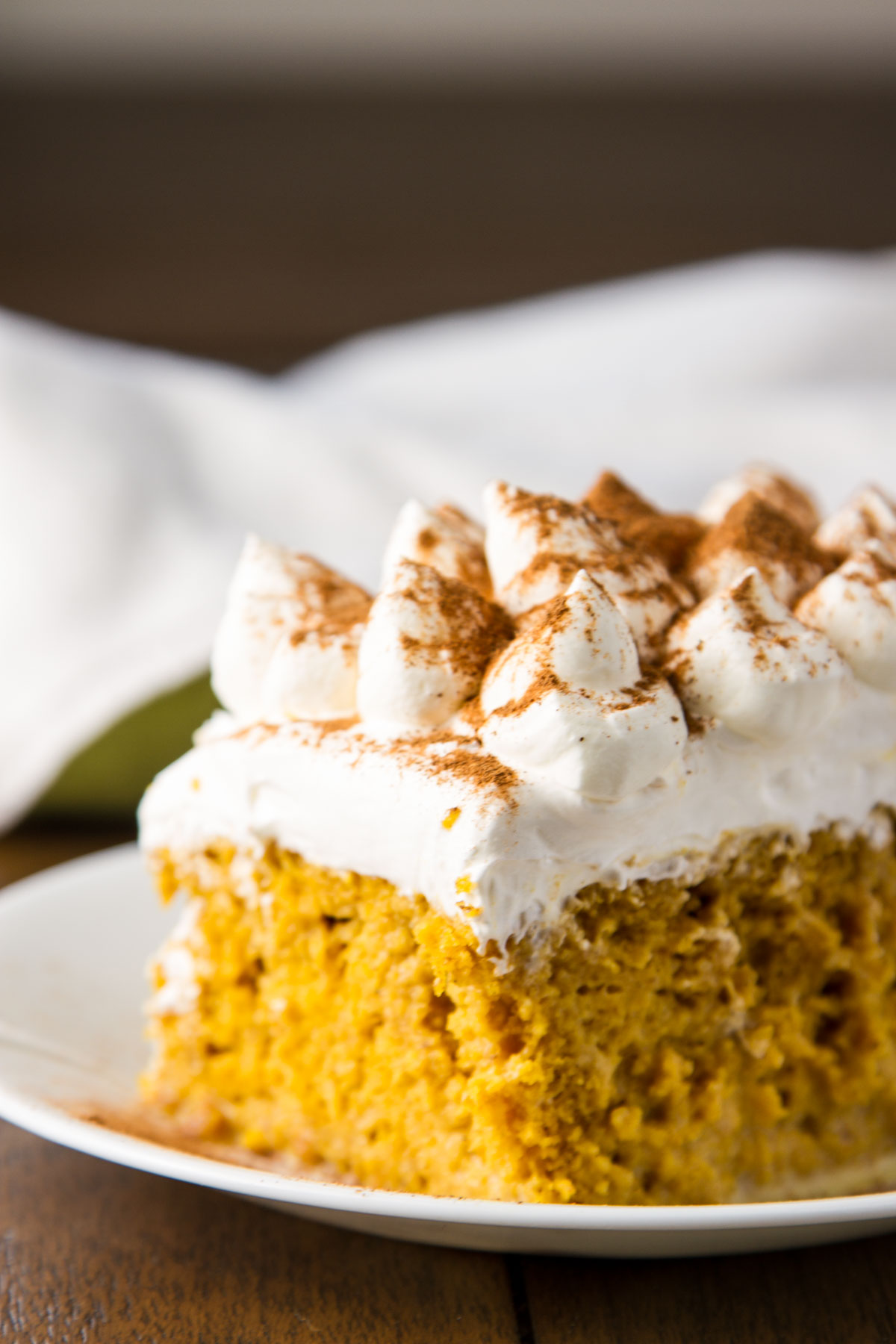 a slice of pumpkin tres leches cake on a small white plate on a wood table next to two vintage colored towels