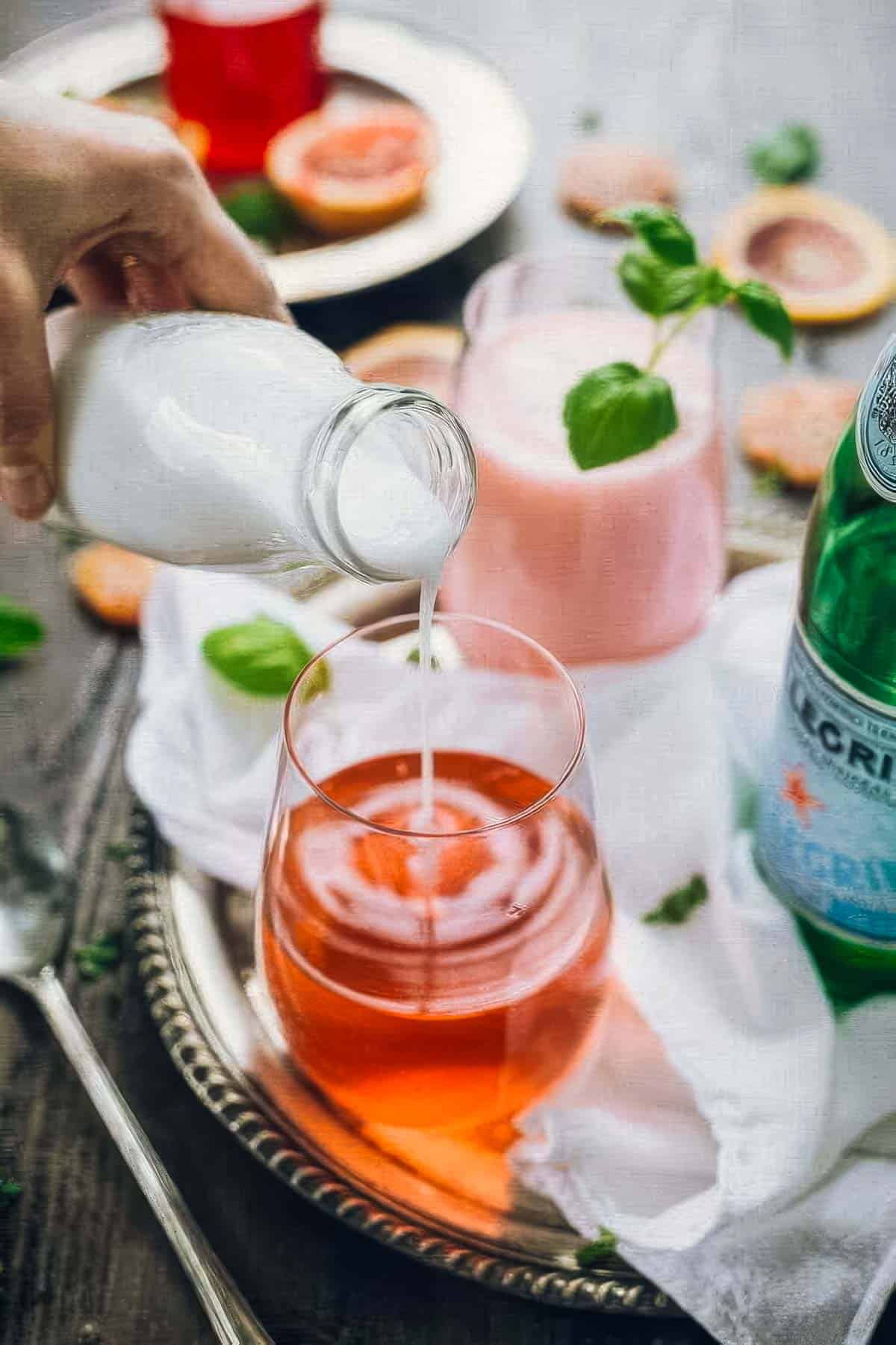 step five in how to make italian blood orange soda: coconut milk being poured into a glass of blood orange syrup and pellegrino