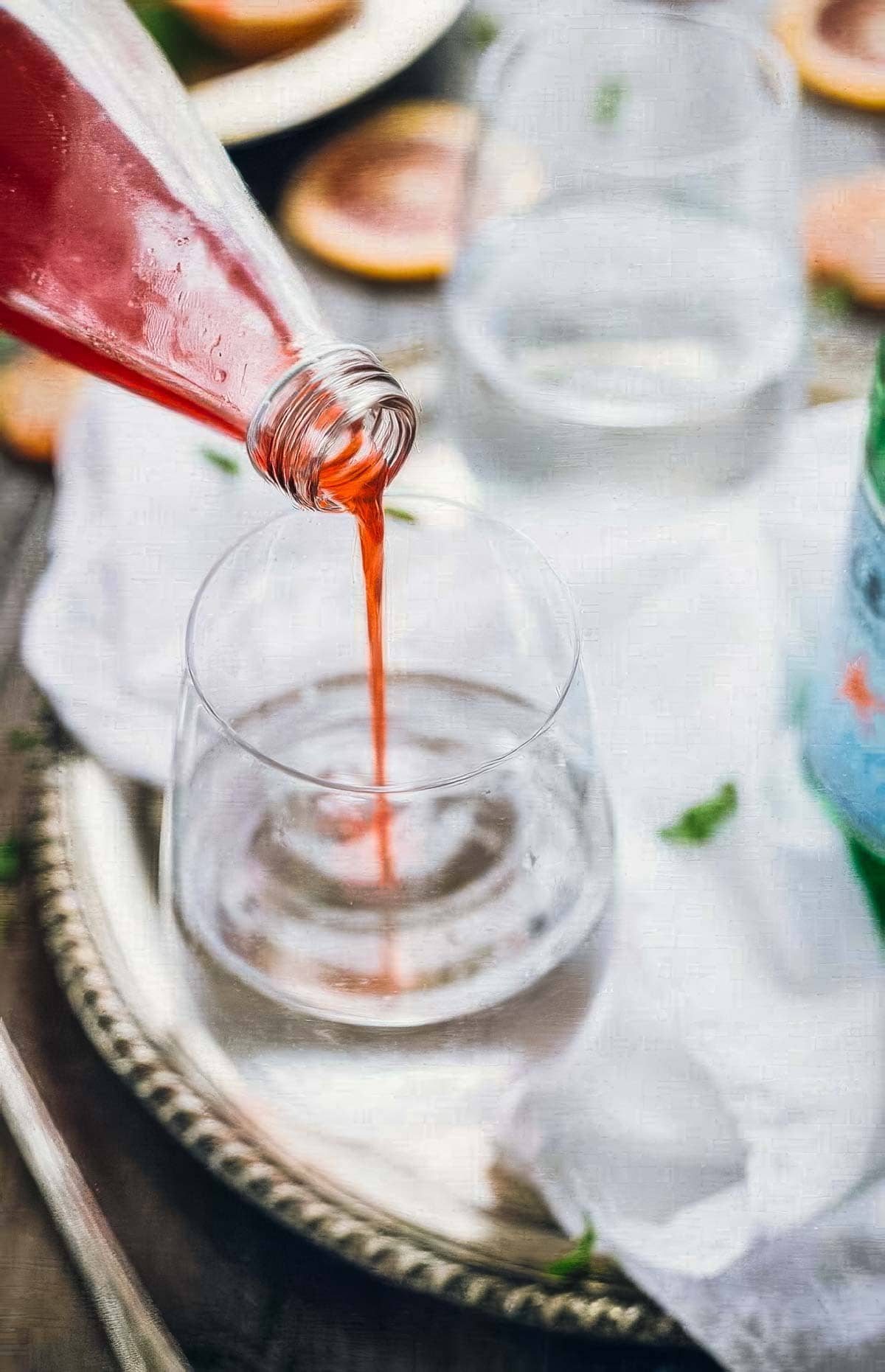 step four in how to make italian blood orange soda: blood orange simple syrup being poured into a glass of pellegrino