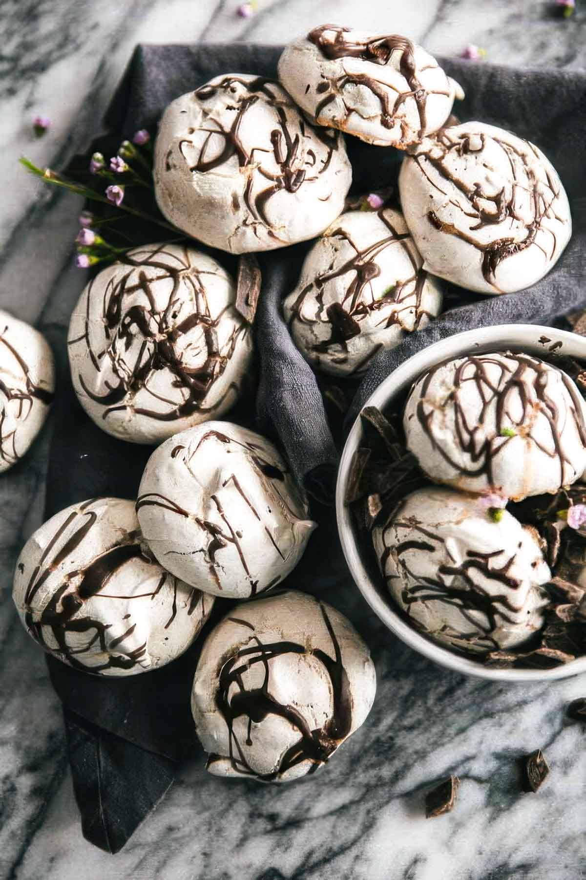 a white bowl filled with swirled chocolate meringue cookies with more cookies on a linen towel on the table around the bowl