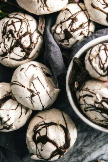 a white bowl filled with chocolate meringue cookies with more cookies on a linen towel on the table around the bowl