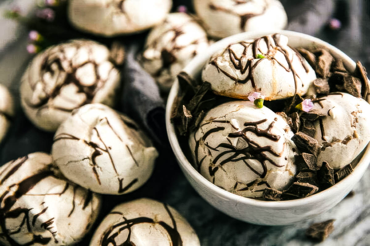 a white bowl filled with swirled chocolate meringue cookies with more cookies on a linen towel on the table around the bowl