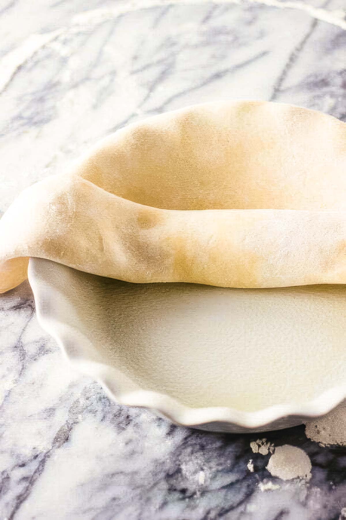 Step seven to making a homemade pie crust: half of a rolled pie crust being added to the pie pan