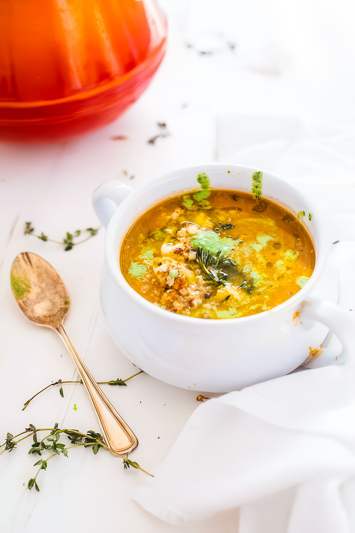 a white bowl filled with roasted cauliflower tomato soup next to a vintage spoon and fresh thyme
