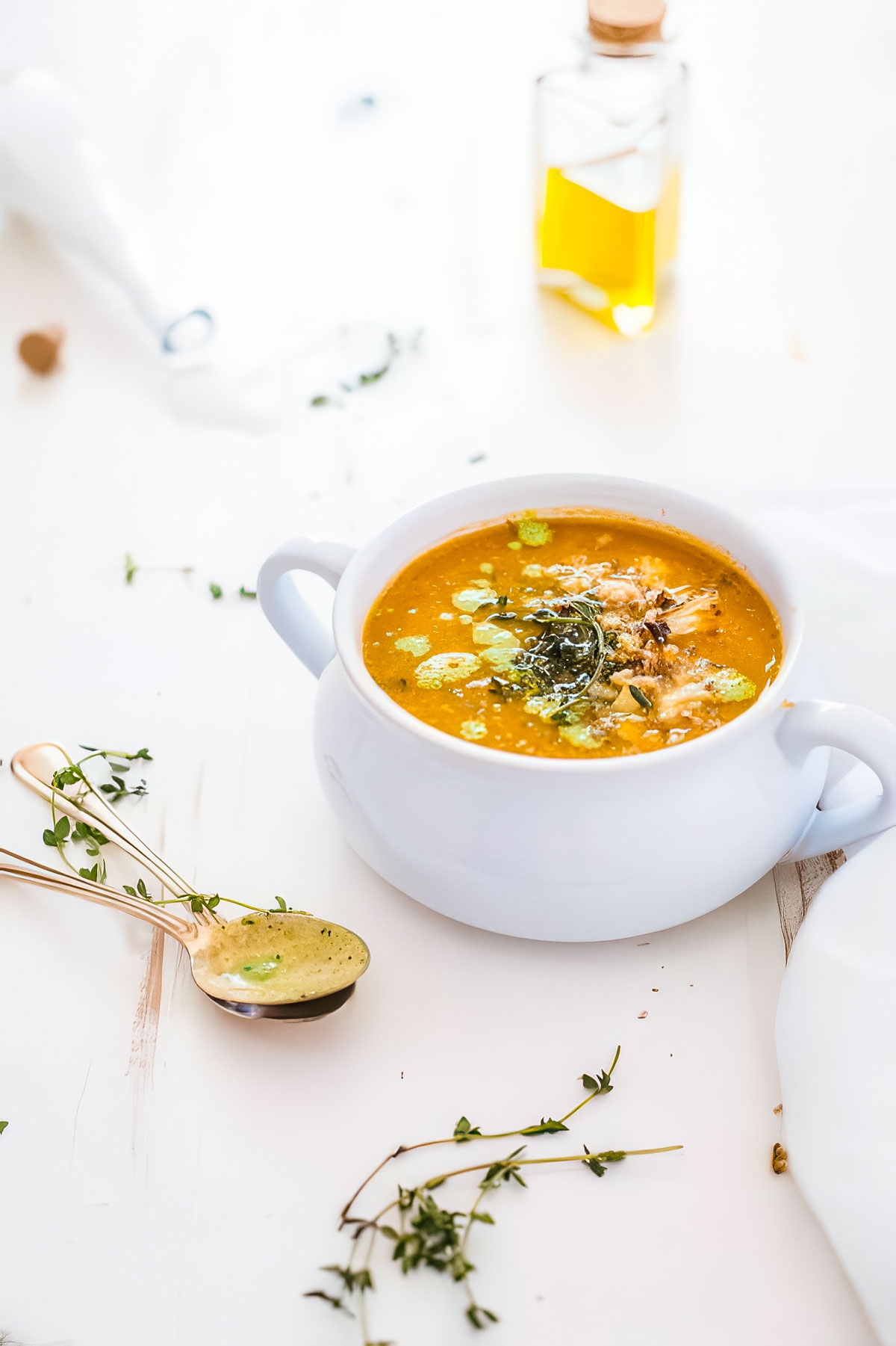 a white bowl filled with roasted cauliflower tomato soup next to a vintage spoon and fresh thyme