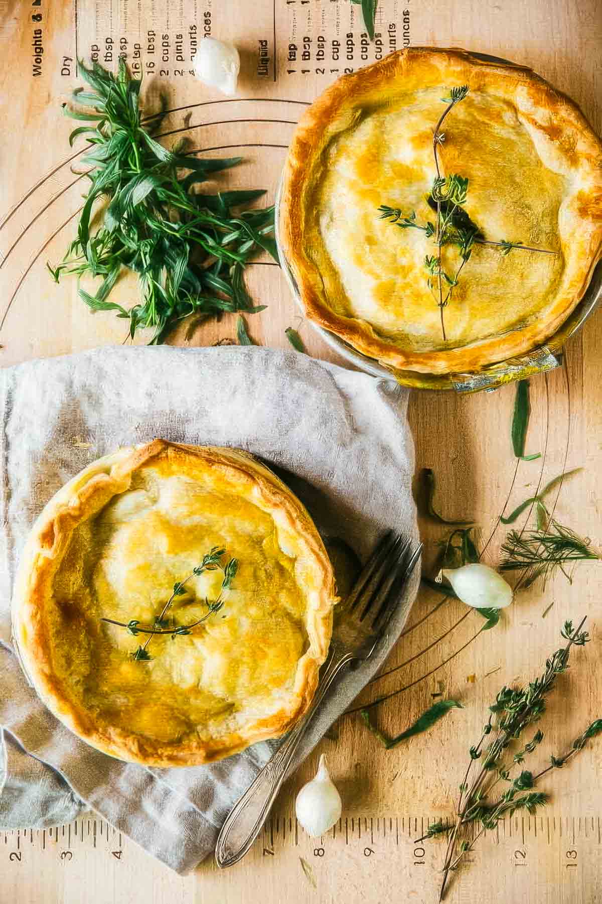 two veggie pot pies just out of the oven with a golden brown crust and garnished with fresh thyme sprigs next to a pile of fresh herbs