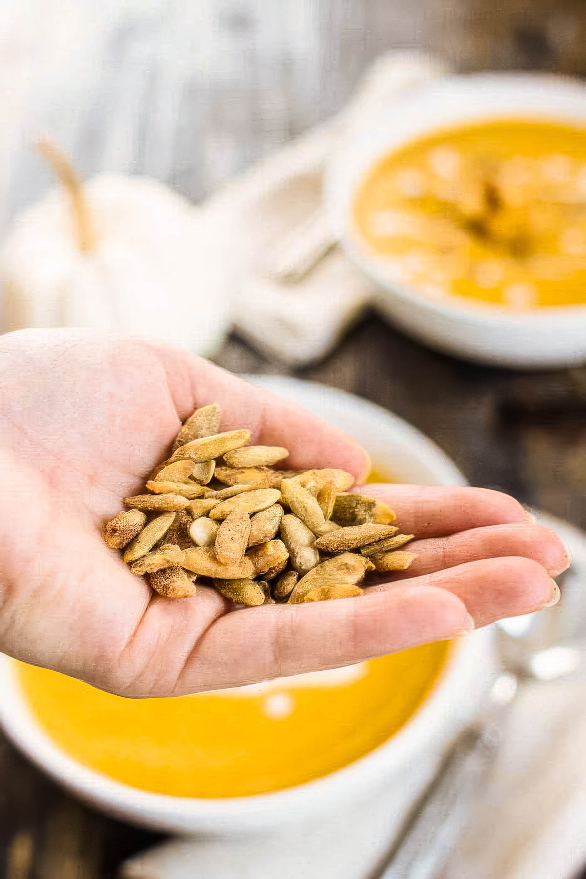 Butternut Squash and Sweet Potato Soup a person's hand holding roasted pumpkin seeds above a white bowl filled with butternut squash and sweet potato soup