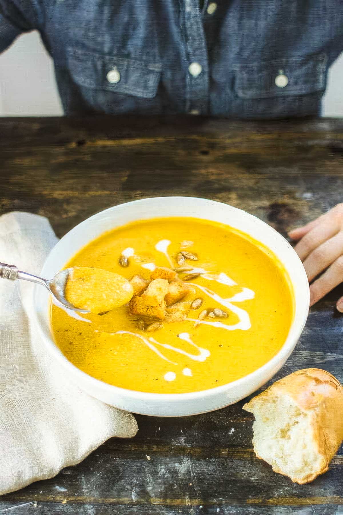 Butternut Squash and Sweet Potato Soup a person sitting at a table about to take a spoonful from a white bowl filled with butternut squash and sweet potato soup