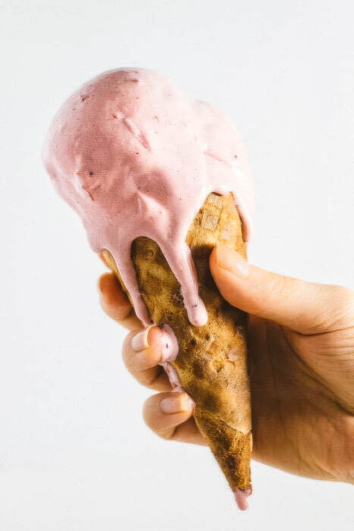 an ice cream cone filled with cranberry ice cream, dripping down onto the hand that's holding it
