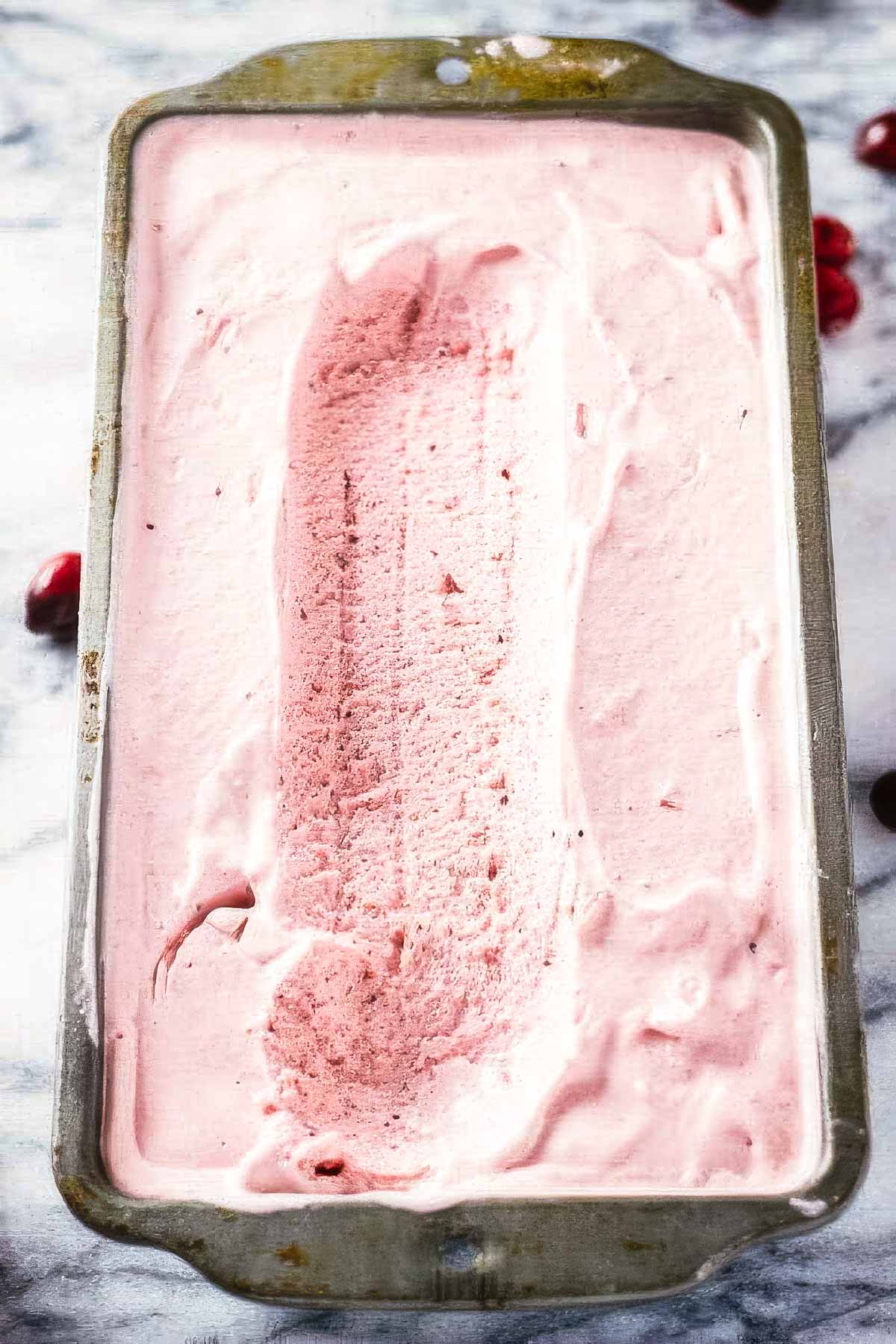 a vintage loaf pan filled with cranberry ice cream with one scoop missing