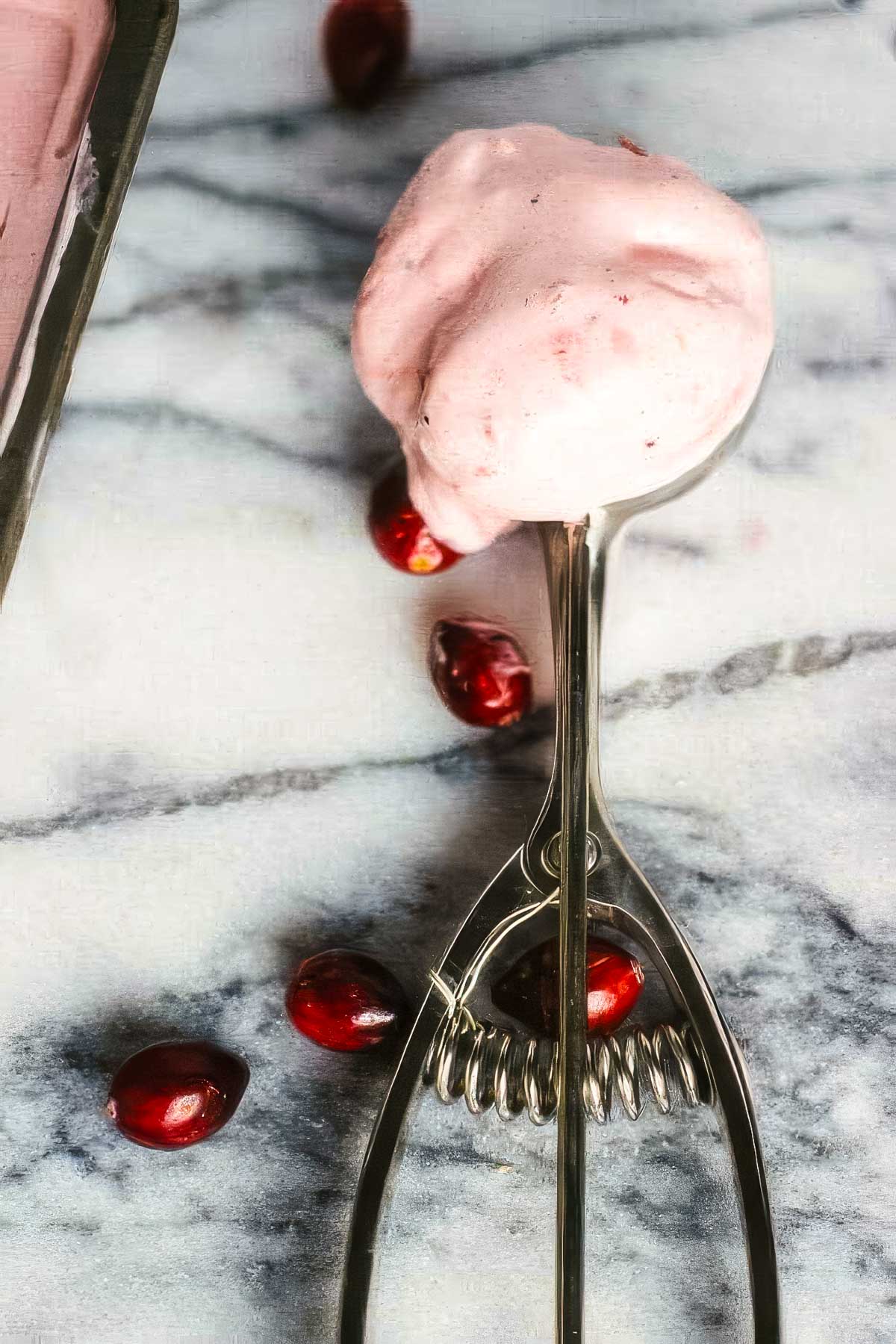 an ice cream scoop filled with cranberry ice cream with some fresh cranberries scattered around it on a marble countertop