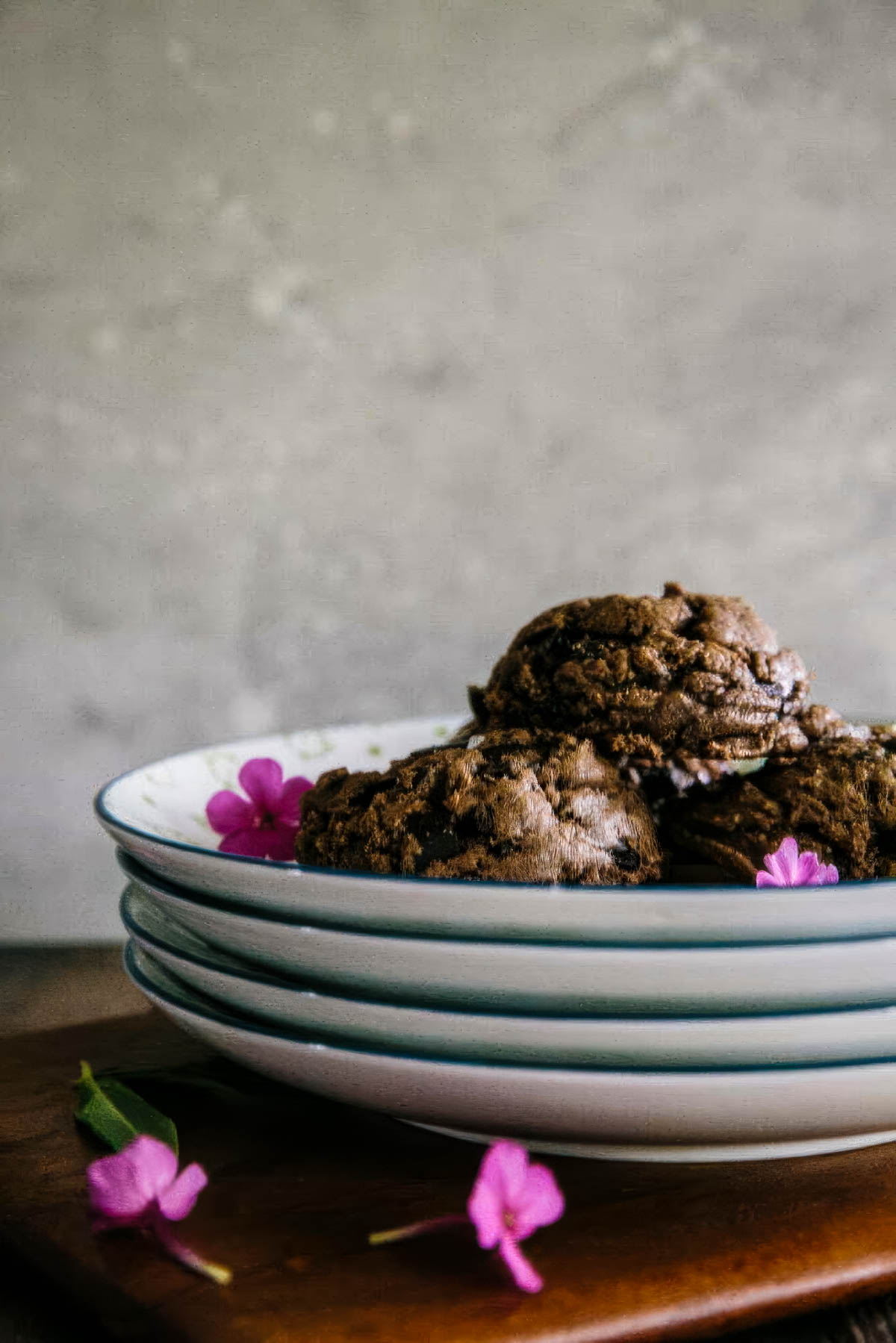 several vintage plates stacked with the top plate filled with double chocolate cookies topped with sea salt