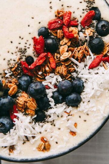 a closeup of a coconut smoothie bowl topped with fresh blueberries, granola, and goji berries