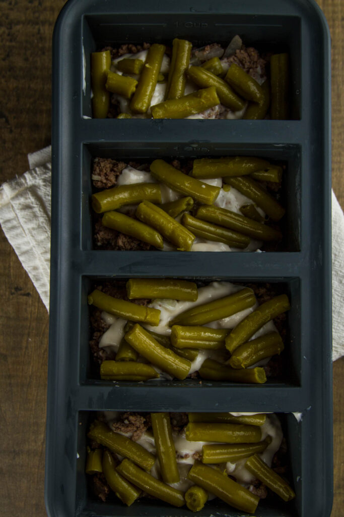 Easy Tater Tot Casserole a 1-cup souper cube tray filled with cooked ground beef, onions, and garlic, cream of mushroom soup, and green beans on top, the third layer in easy tater tot casserole