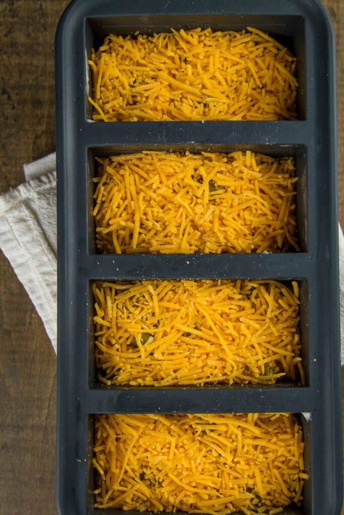 Easy Tater Tot Casserole a 1-cup souper cube tray filled with cooked ground beef, onions, and garlic, cream of mushroom soup, green beans, and shredded cheddar cheese on top, the fourth layer in easy tater tot casserole