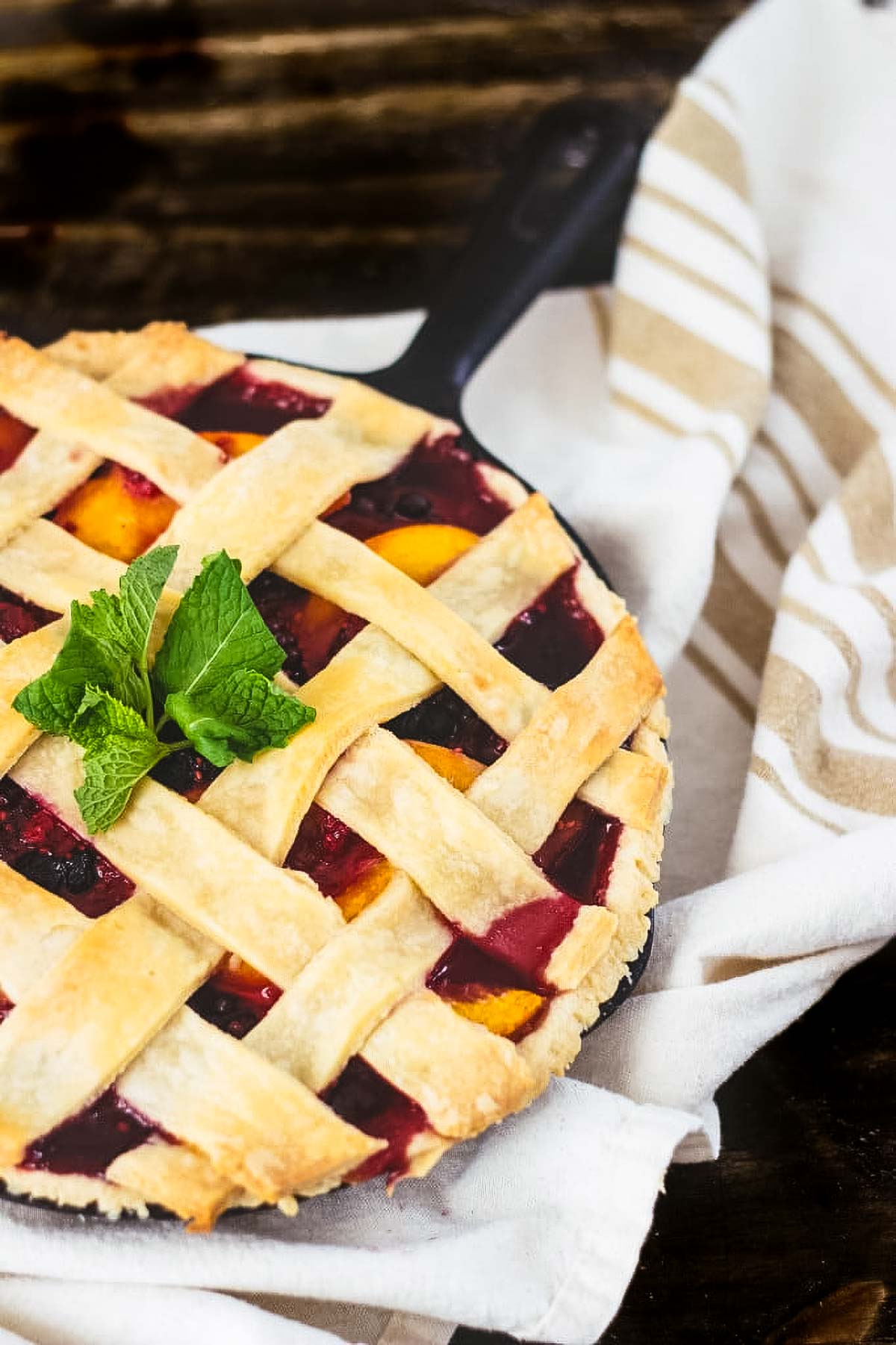 Frozen Berry Pie a frozen berry pie baked in a cast iron skillet just out of the oven on a white kitchen towel on a wood table