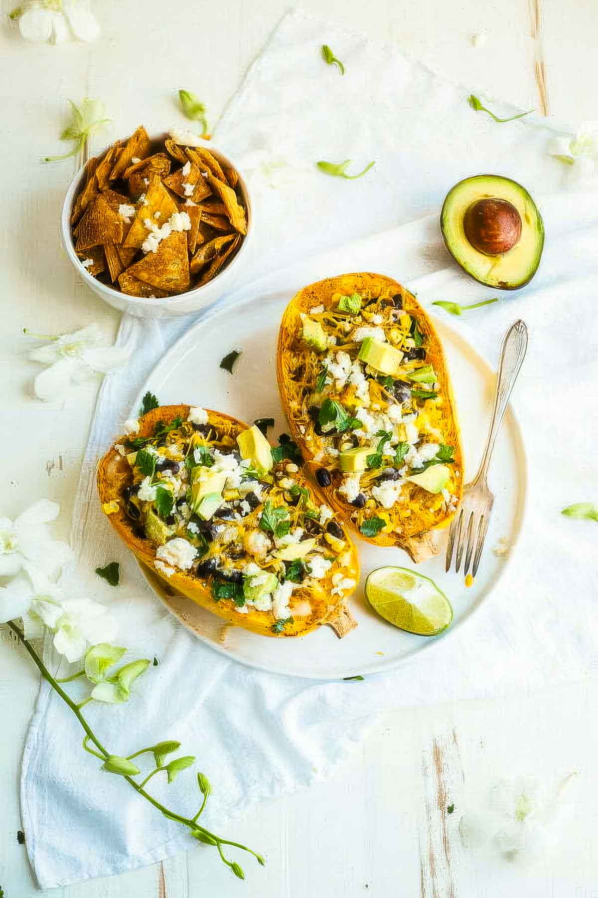 Mexican Spaghetti Squash two mexican spaghetti squash on a white plate next to a halved avocado and a bowl of tortilla chips