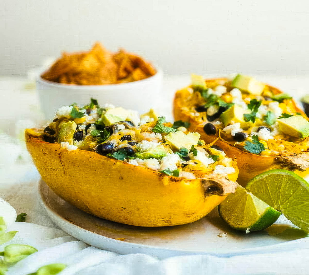 Mexican Spaghetti Squash a side view of two mexican spaghetti squash on a white plate with a small bowl of tortilla chips in the background