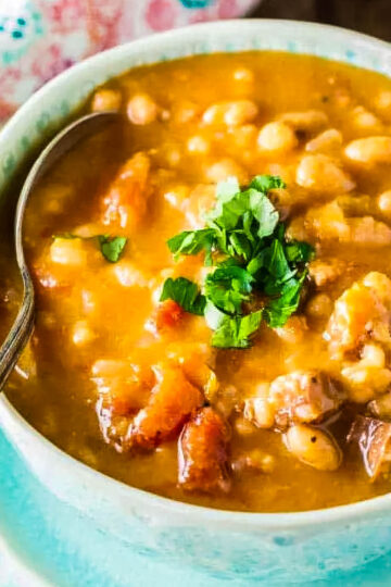 a side view of sausage bean soup with a spoon and garnished with chopped fresh parsley