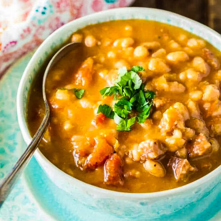 a side view of sausage bean soup with a spoon and garnished with chopped fresh parsley