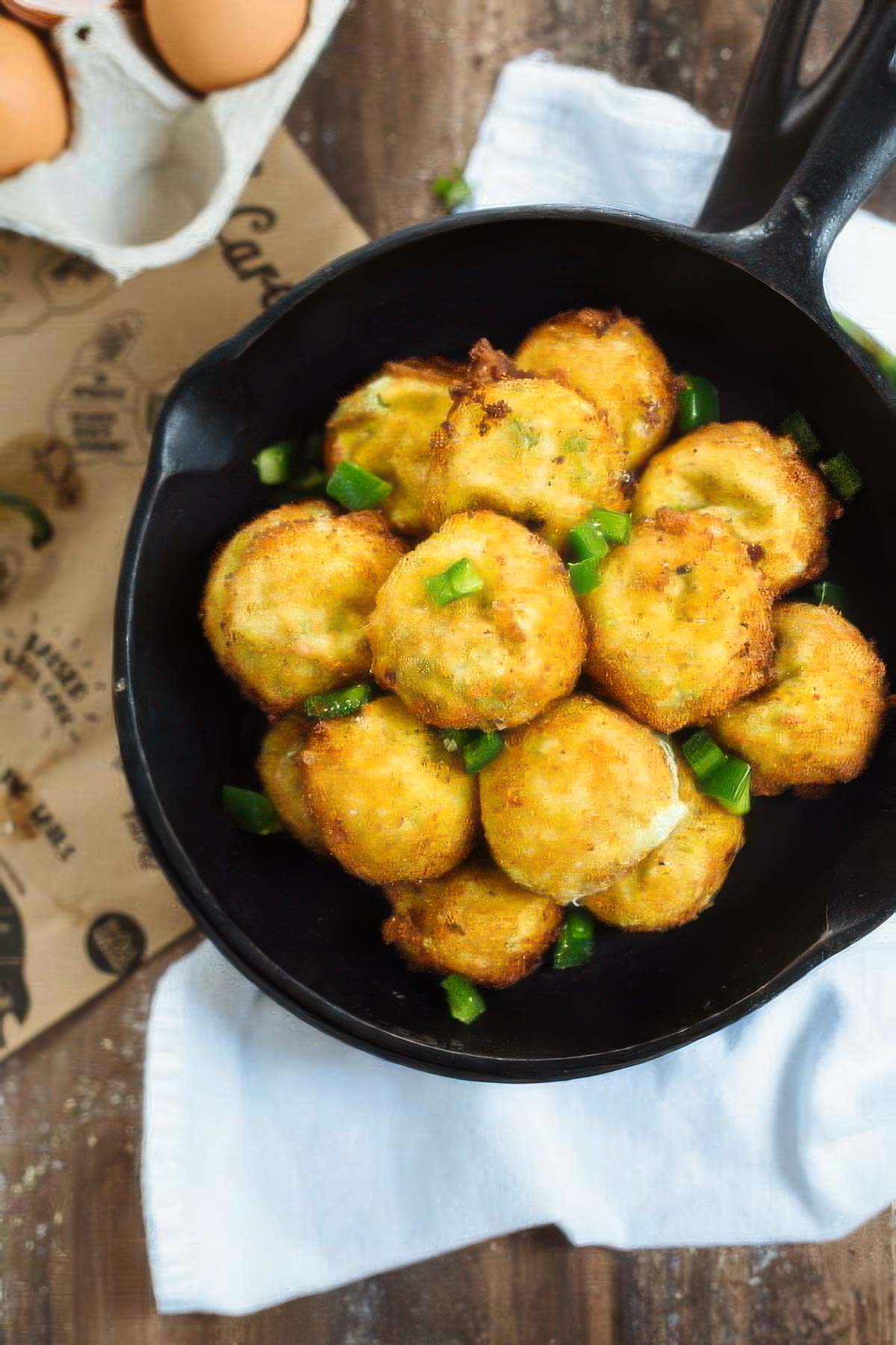 a pan of spicy cheese fritters on a white towel on a wood table