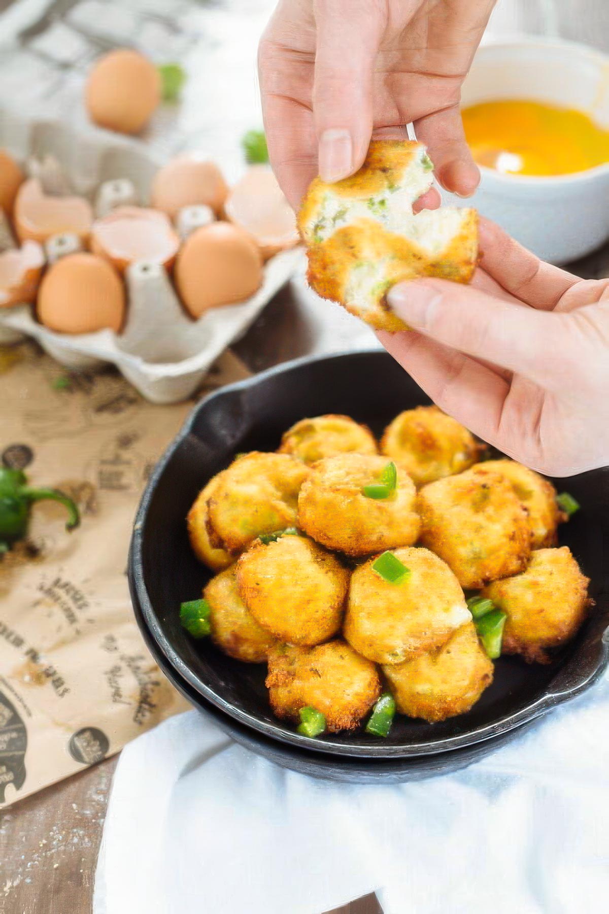 Spicy Cheese Fritters - Deep or Air Fry a hand holding a spicy cheese fritter being pulled apart with a pan of them sitting on a table in the background