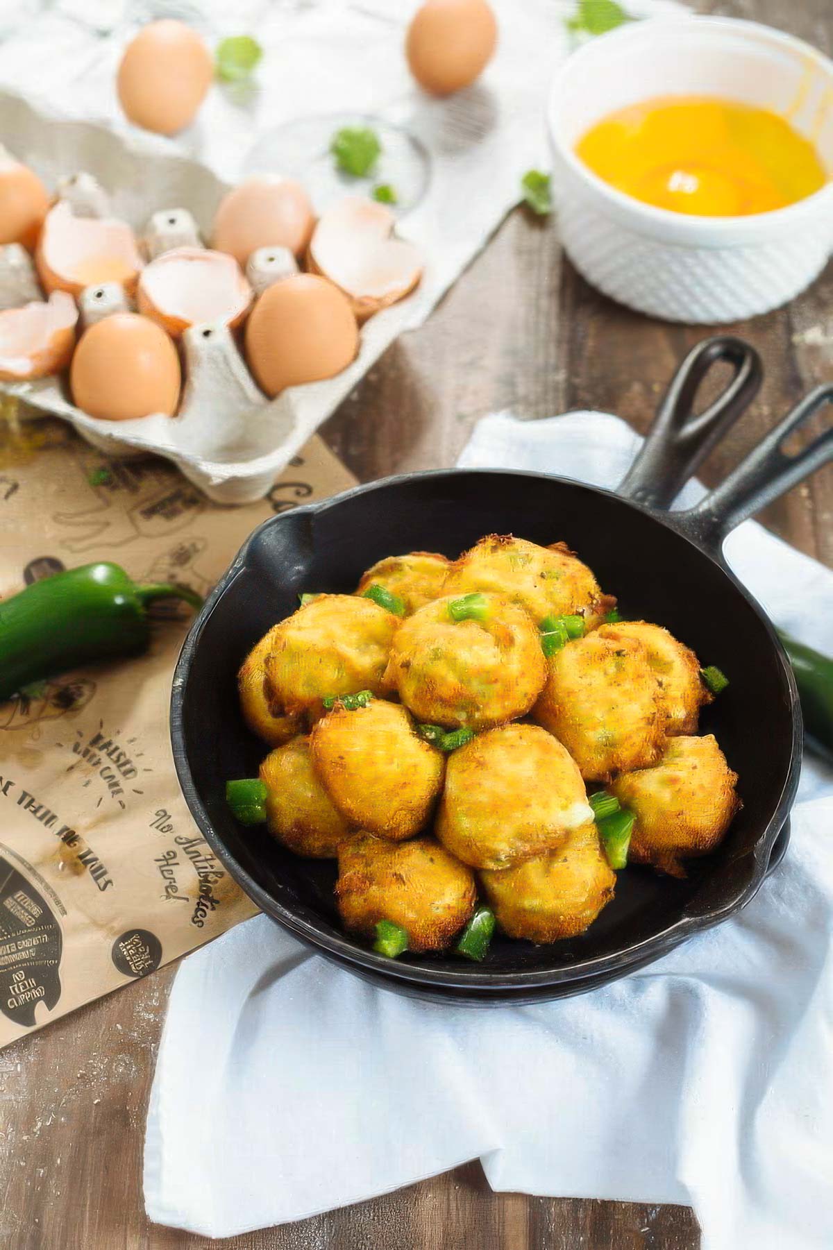 Spicy Cheese Fritters - Deep or Air Fry a pan of spicy cheese fritters on a white towel next to fresh eggs and a fresh jalapeño