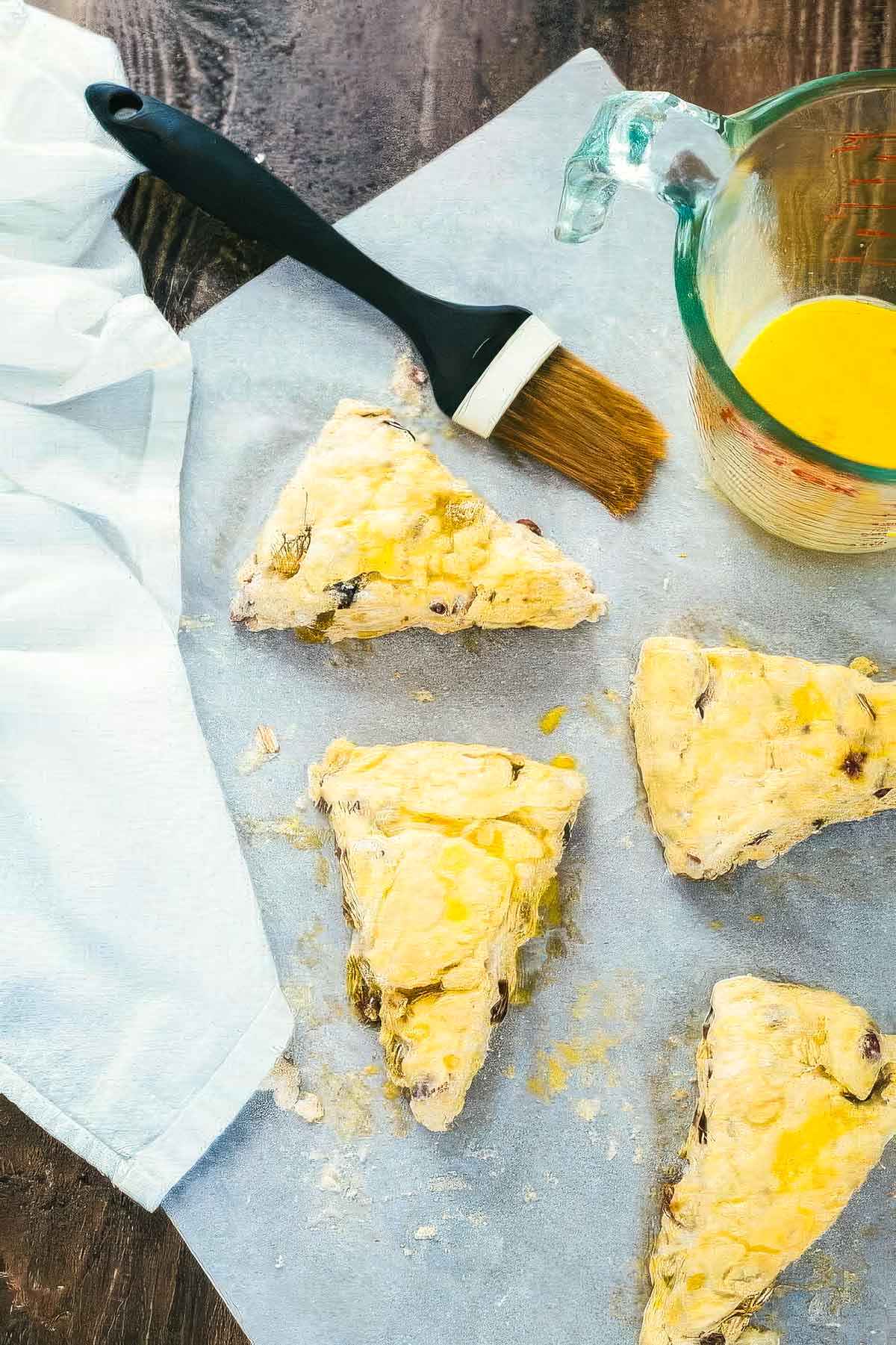 Irish Soda Bread Scones with Cinnamon Honey Butter step 7 when making irish bread scones: unbaked scones on parchment paper next to a small dish of beaten egg and a pastry brush for brushing the egg onto the scones