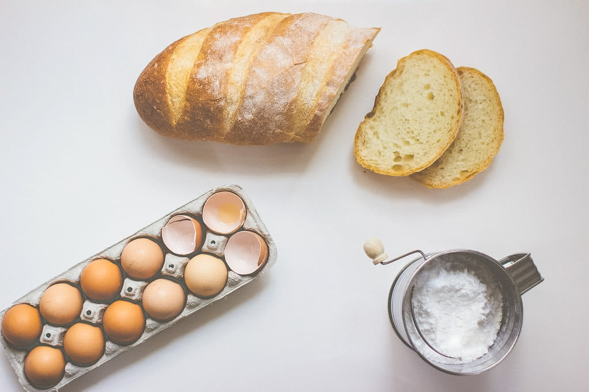 Sourdough French Toast with Mascarpone a sourdough baguette, an open carton of fresh eggs, and powdered sugar showing the ingredients needed to make sourdough french toast
