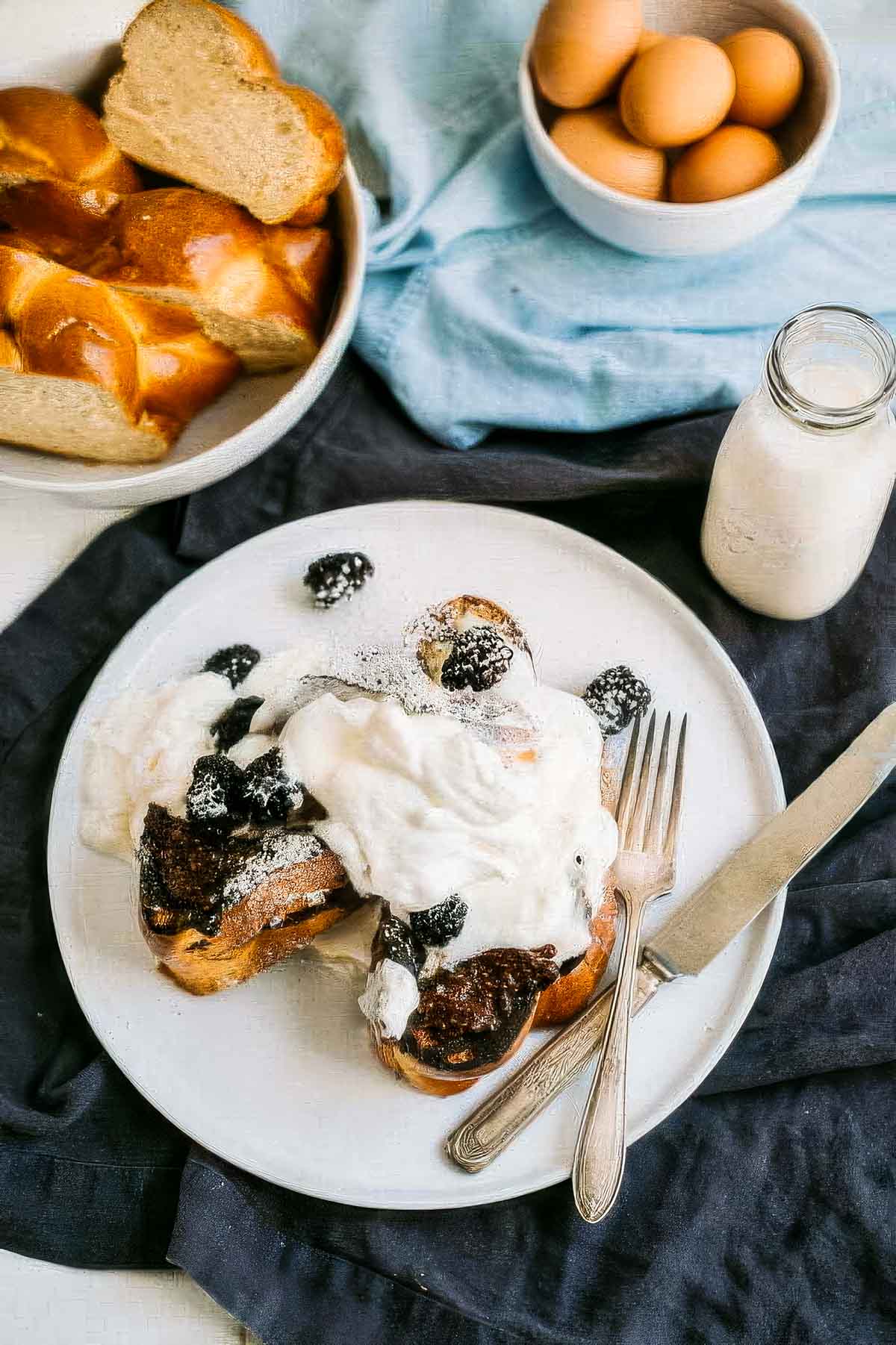 Sourdough French Toast with Mascarpone a stack of sourdough french toast on a black plate topped with fresh berries and mascarpone cream with one bite taken out