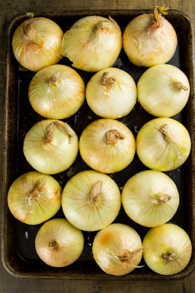 Whole Oven Roasted Onions (+ 33 Ways to Use Them!) step 3 when making whole oven roasted onions: a sheet pan filled with whole onions after having been drizzled with olive oil