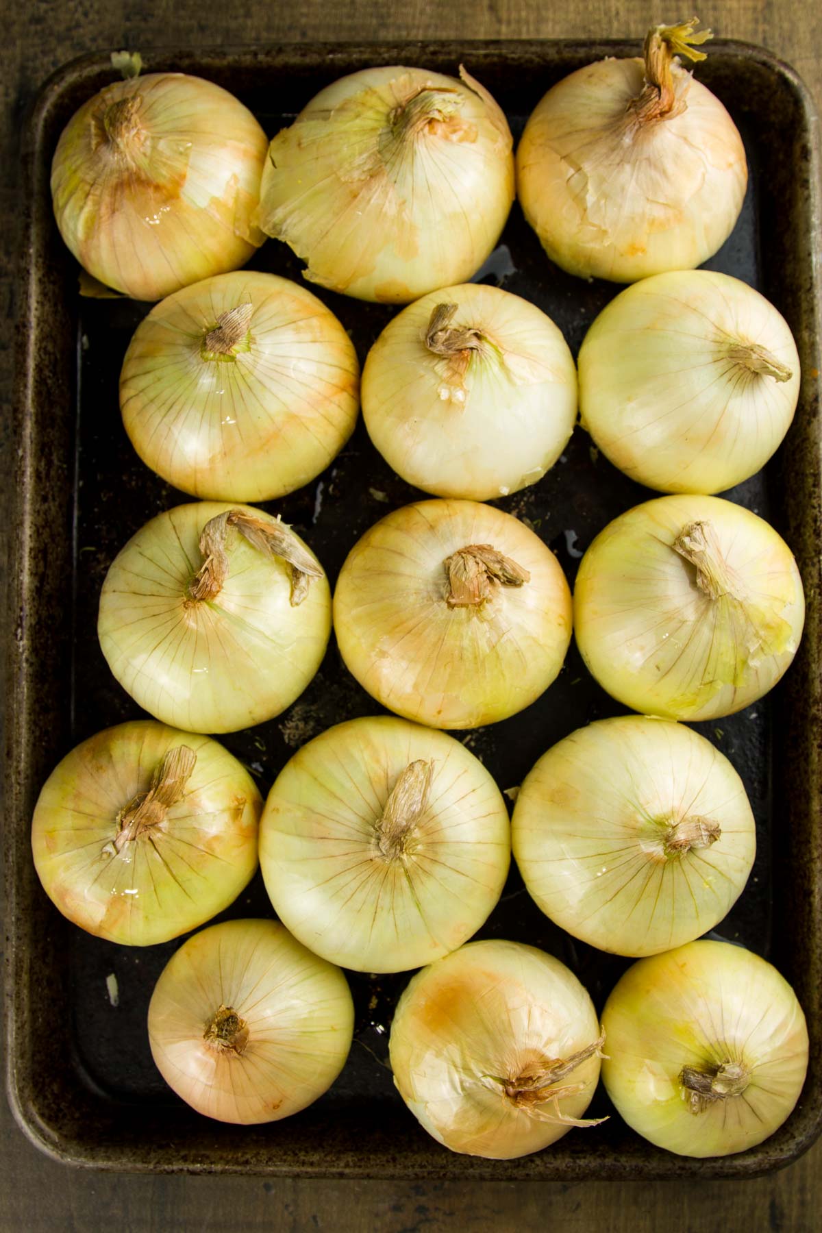 Whole Oven Roasted Onions (+ 33 Ways to Use Them!) step 3 when making whole oven roasted onions: a sheet pan filled with whole onions after having been drizzled with olive oil