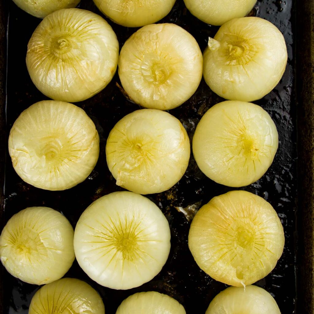 Whole Oven Roasted Onions (+ 33 Ways to Use Them!) step 6 when making whole oven roasted onions: a sheet pan filled with whole oven roasted onions after they've cooled and the skins have been removed, the tops cut off, and they're ready to be enjoyed
