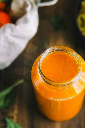 a jar of authentic italian marinara sauce next to a bowl of cooked pasta and a bowl of tomatoes on the vine