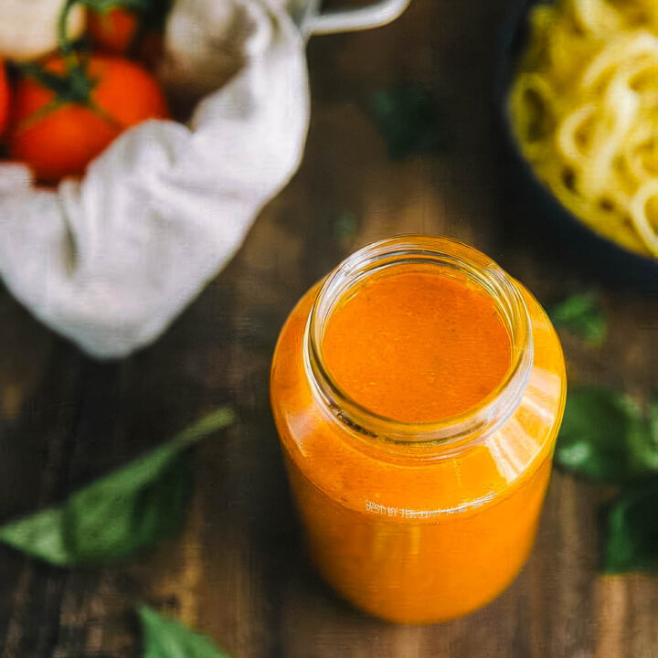 a jar of authentic italian marinara sauce next to a bowl of cooked pasta and a bowl of tomatoes on the vine