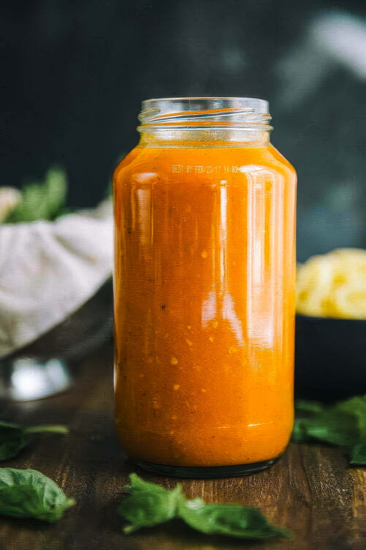 Authentic Italian Marinara Sauce a jar of authentic italian marinara sauce with bowls of cooked pasta and fresh basil in the background