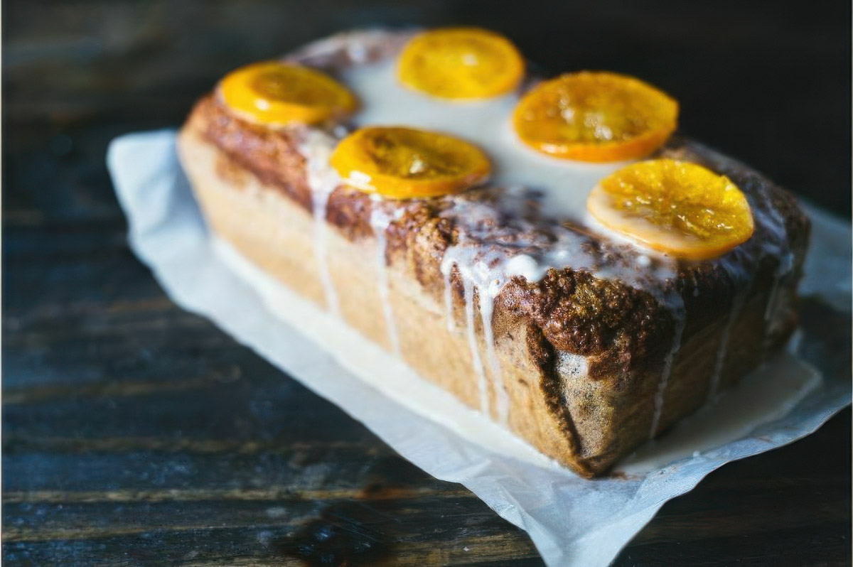 a clementine quick bread recipe showing the completed loaf dripping with icing and topped with candied clementines