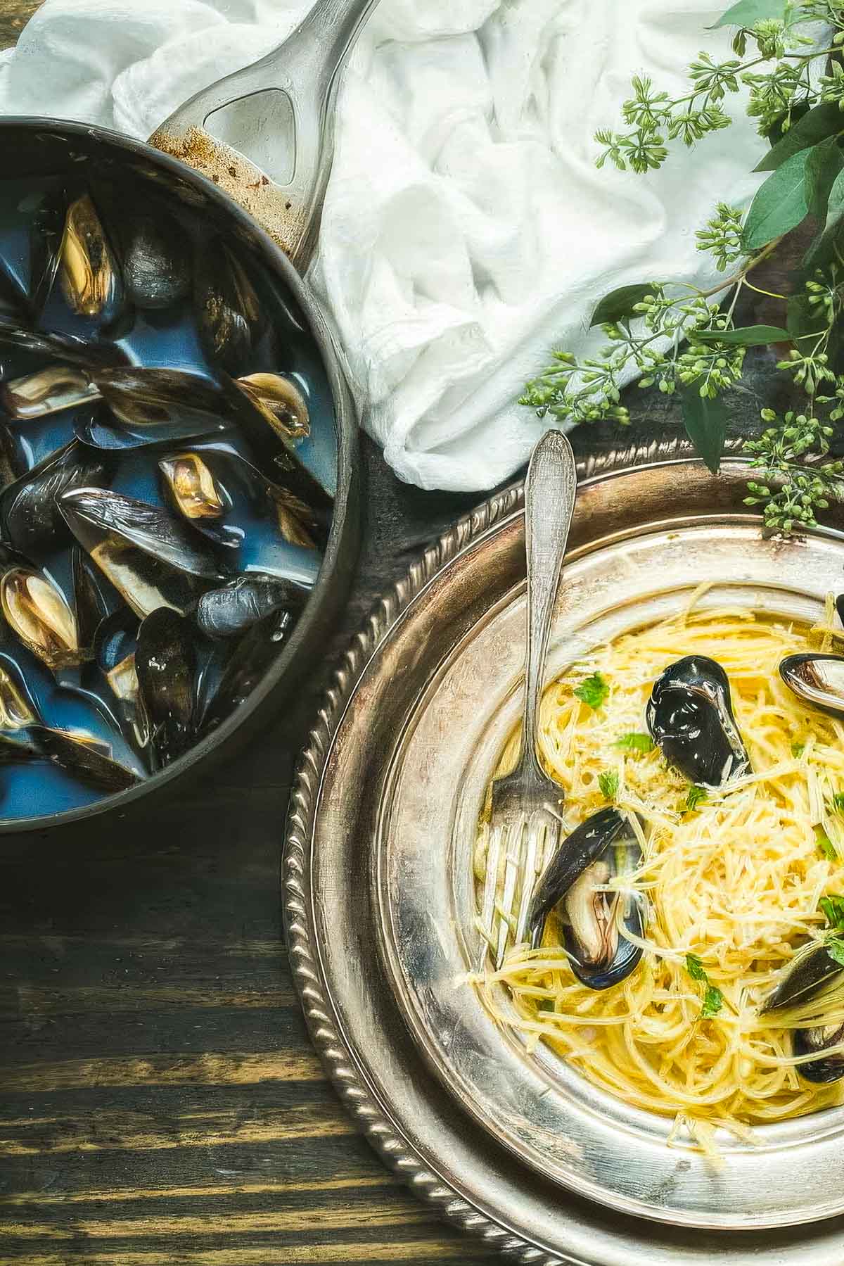 overhead shot of Mussels carbonara on a vintage plate with a fork and fresh greens and a white towel